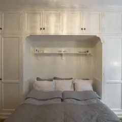 En inbäddad säng med grå täcken och vita kuddar, omgiven av vita skåp som utstrålar en tidlös, old money aesthetic.