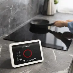 Cocina moderna con vitrocerámica y tablet para controlar electrodomésticos inteligentes. Una persona cocina en la placa de inducción.