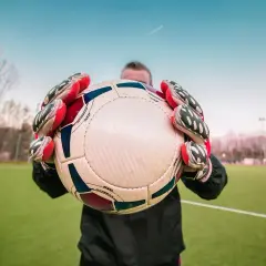 Bramkarz w rękawicach trzyma piłkę na boisku piłkarskim.