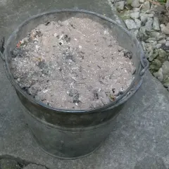 Metalowy kubeł wypełniony popiołem z węgla, który może posłużyć jako cenny nawóz do ogrodu.