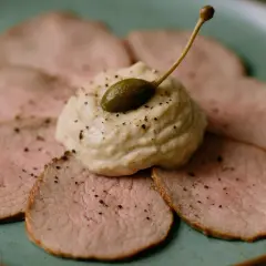Vitello Tonnato auf einem Teller, garniert mit Kapern und einer cremigen Sauce. Perfekt zu einem Glas Weißwein.