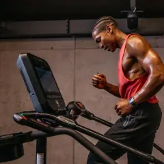 Schweißglänzender Mann im roten Tanktop gibt alles beim liss cardio auf dem Laufband.