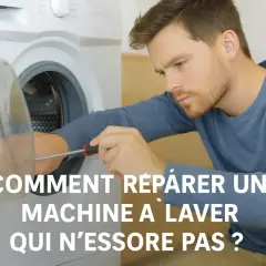Un homme répare une machine à laver qui n'essore plus. Il utilise un tournevis pour examiner le tambour.
