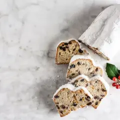 Le stollen, un délice de Noël, est saupoudré de sucre glace. Des tranches révèlent des fruits secs et des baies rouges sur une branche de houx.