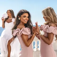Trzy kobiety w cudownych sukienkach na wesele, dwie w pudrowych, jedna w białej, pozują na tle morza.