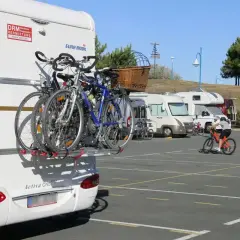 Camping-car avec vélos à l'arrière. Un cycliste s'entraîne sur un parking. Avis sur aire de camping-car.