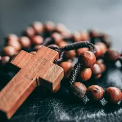 Drewniany krzyż i paciorki różańca, symbolizujące dziesiątkę różańca jako pokutę, leżą na ciemnej powierzchni.