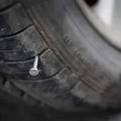 Un clou rouillé est planté dans la bande de roulement d'un pneu usé, annonçant une crevaison imminente.