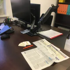 Biurko z laptopem, monitorem, kalkulatorem, gazetą "Gazeta Podatkowa" i wizytówkami.