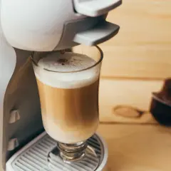 Kawa w kapsułkach: czy jest zdrowa? Ekspres przygotowuje latte, obok leży kapsułka.