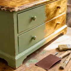 Un meuble ancien customiser, en cours de restauration, avec des outils de peinture et de ponçage.