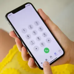 Dłoń trzyma smartfon z klawiaturą numeryczną. Możliwość wykonywania połączeń przez Wi-Fi ułatwia kontakt.
