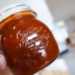 En hand håller ett glas med söt och syrlig rabarberchutney.