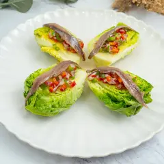Cuatro cogollos de lechuga rellenos de pimientos y cebolla picados, coronados con anchoas. Un bocado fresco y sabroso.