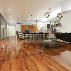 Nowe, lśniące panele podłogowe w ciepłym odcieniu drewna dodają elegancji nowoczesnemu salonowi z aneksem kuchennym. Idealne, by wiedzieć, jakie panele podłogowe wybrać.