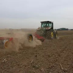 Traktor z agregatem uprawowym wykonuje uprawę bezorkową, wzbijając tumany kurzu na polu.