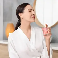 Kobieta w szlafroku rozpyla perfumy. Mgiełka od perfum różni się intensywnością zapachu i trwałością.
