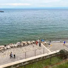 Spacerem po wybrzeżu w Słowenii Piran. Widać łódź na morzu i kilka osób odpoczywających na kamienistej plaży.