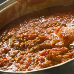 Salsa boloñesa burbujeante en una olla, con una cuchara de madera removiendo la carne picada y los tomates.