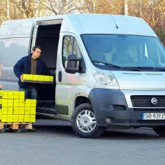 Mężczyzna rozładowuje żółte paczki z Fiata Ducato 2.3.