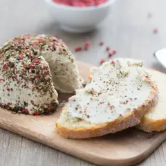 Queso vegano cubierto de pimienta y hierbas, servido en rebanadas de pan rústico.
