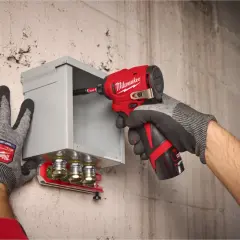 Ręce w rękawicach trzymają czerwoną zakrętarkę udarową, która wkręca śrubę w metalową skrzynkę. Czy zakrętarka udarowa można wiercić? Tak, to narzędzie jest wszechstronne.