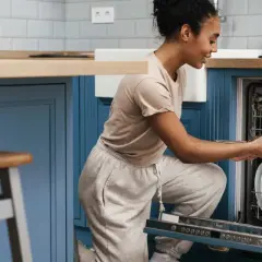 Une femme charge son lave-vaisselle encastrable. Elle place une casserole dans le panier inférieur.