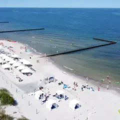 Słoneczny weekend majowy nad morzem. Ludzie odpoczywają na plaży, kąpią się w morzu i opalają pod białymi parasolami.