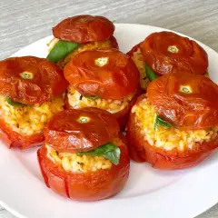 Sei pomodori ripieni di riso e basilico, cotti al forno, su un piatto bianco.