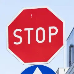 Czerwony znak stop z białym napisem. Obok nowoczesny budynek.