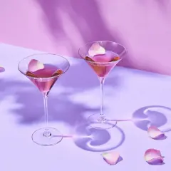 Dwa kieliszki z różowym drinkiem, ozdobione płatkami róż. Cienie liści tworzą romantyczną atmosferę, jak z bajki o ciociosan.