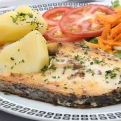 Un succulento pesce spada al forno, servito con patate bollite, pomodori a fette, carote grattugiate e insalata fresca.