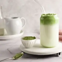 Zielony napój z mlekiem i słomką, obok miseczka z proszkiem. To właśnie co to matcha – aromatyczny napój z zielonej herbaty.