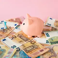 Różowa świnka-skarbonka na stosie banknotów euro. Zastanawiasz się nad oprocentowaniem konta walutowego?