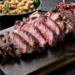 Côte de bœuf juteuse, tranchée et prête à être dégustée. Parfaitement cuite sur la plancha, accompagnée de haricots et de poivre rose.