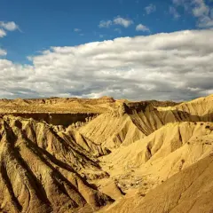 Paisaje árido y erosionado del Desierto de Tabernas, con barrancos y formaciones rocosas bajo un cielo azul con nubes. ¡Un lugar ideal para visitar!