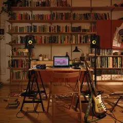Bureau de musique avec ordinateur affichant un logiciel comme FL Studio, enceintes, guitare et microphones, entouré d'étagères remplies de livres.
