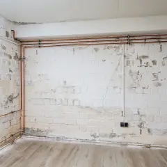 Undichte Dachrinne verursacht nasse Wand. Putz bröckelt, Kupferrohre verlaufen entlang der weißen Ziegelwand.