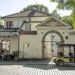Urokliwy dzień w dzielnicy Kazimierz w Krakowie. Przy bistro barze siedzą ludzie, a obok bramy z hebrajskimi napisami stoi żółty meleks.