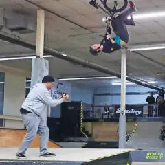 BMX-Fahrer vollführt einen Salto in der Luft in der Wicked Woods Wuppertal. Ein Mann filmt den Stunt.