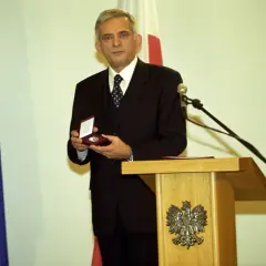Jerzy Buzek, premier Polski, prezentuje medal. Obok flagi NATO i Polski.