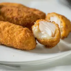 Croquetas de bacalao doradas y crujientes, una partida muestra su interior jugoso y blanco.