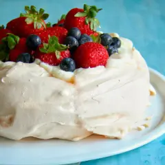 Deliciosa pavlova receta original, coronada con fresas y arándanos frescos, sobre una base de merengue crujiente y crema batida.