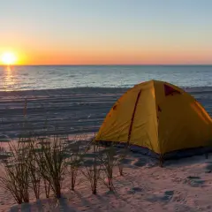 Żółty namiot na piaszczystej plaży, z widokiem na spokojne morze i zachodzące słońce. Idealne miejsce na nocleg, gdzie pole namiotowe nad morzem wita o poranku.