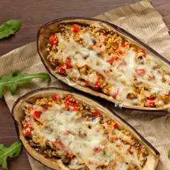 Dos mitades de berenjenas rellenas con cuscús, pimientos y queso derretido, cocinadas en airfryer.