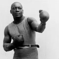 A boxer in an old boxing stance, wearing a tank top and shorts, with gloves on both hands, ready to fight.