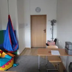 Przytulny gabinet pedagoga szkolnego z kolorowym workiem sako w kształcie ptaka, huśtawką i biurkiem.