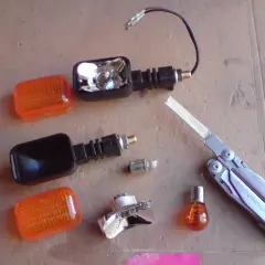 Części do wymiany żarówki kierunkowskazu motocykla: pomarańczowe klosze, obudowy, żarówki, multitool Leatherman Surge.