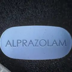 Niebieska tabletka z napisem ALPROZOLAM leży obok białej.