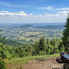 Dwie dziewczynki siedzą przy drewnianym stole, podziwiając rozległą panoramę **Beskidu Makowskiego**. W oddali widać łagodne **szczyty** i malownicze doliny.